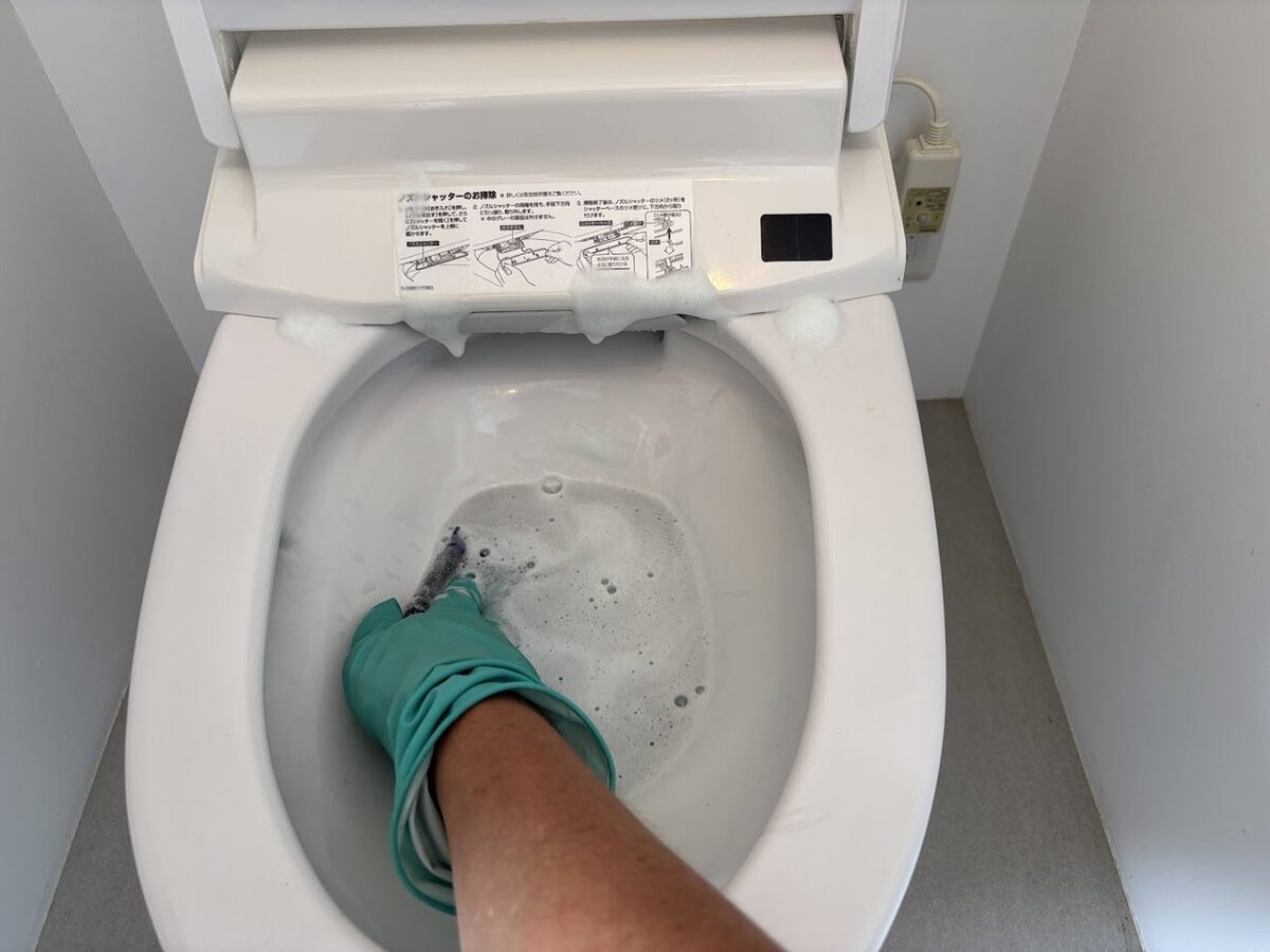 ゴム手袋でトイレの便器内をブラシ洗浄している様子