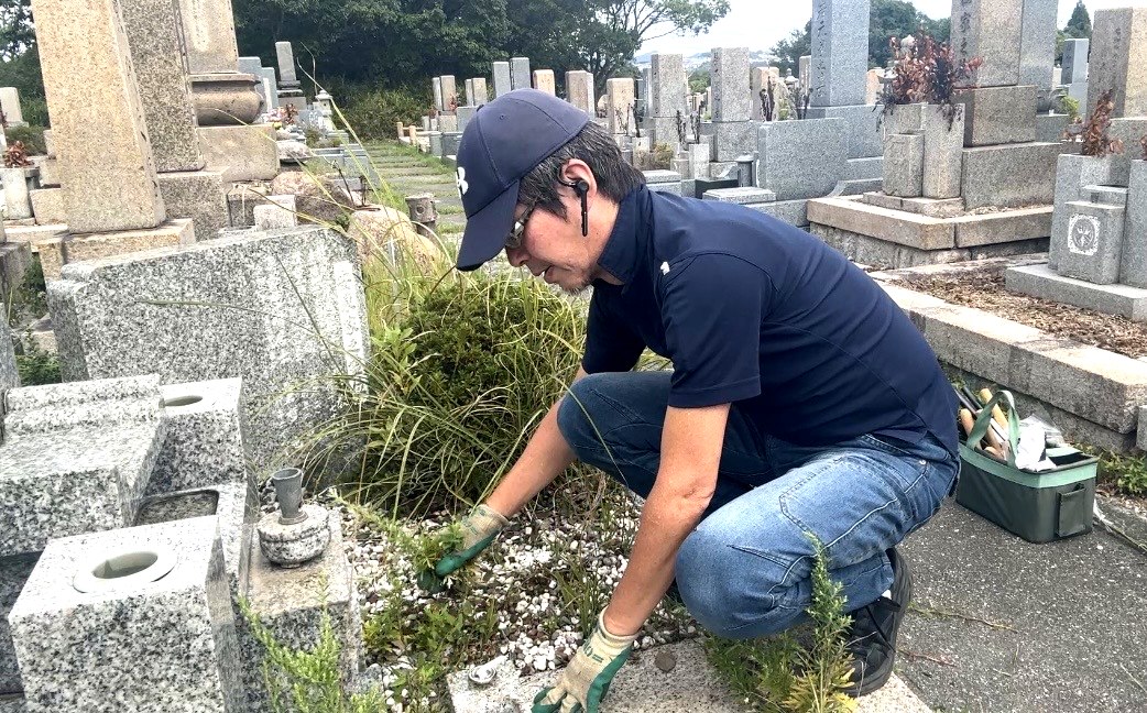 神戸市北区鵯越墓園でしゃがんで根元から雑草を手で引き抜く作業の様子