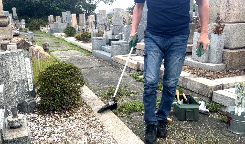 お墓の前の通路を箒で掃き掃除する神戸市北区鵯越墓園でのお墓掃除の仕上げ作業