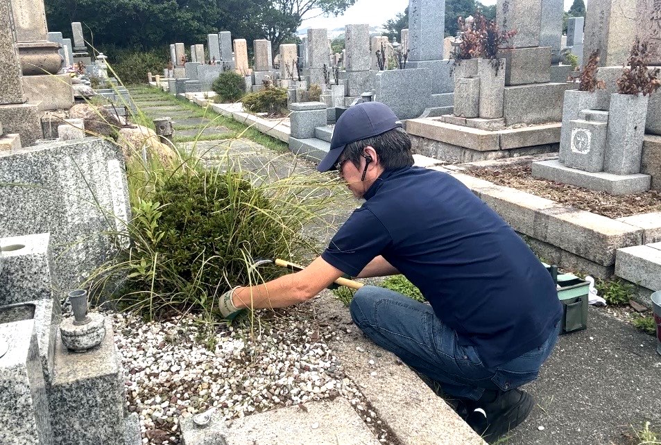柄の長い草取り道具を使って根の張った雑草を除去する神戸市北区のお墓掃除作業