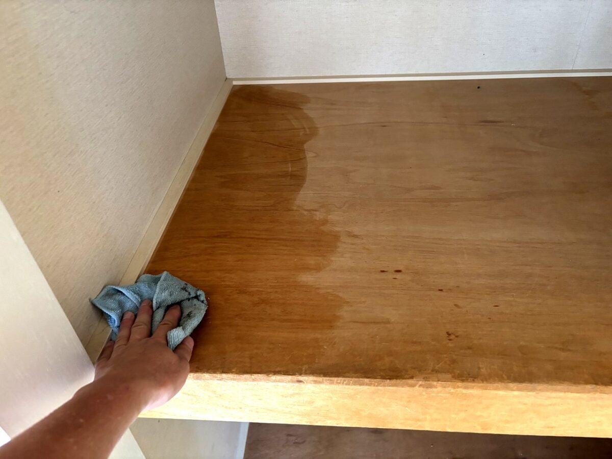 収納棚の天板についたシミを布巾で拭き取っている手元
