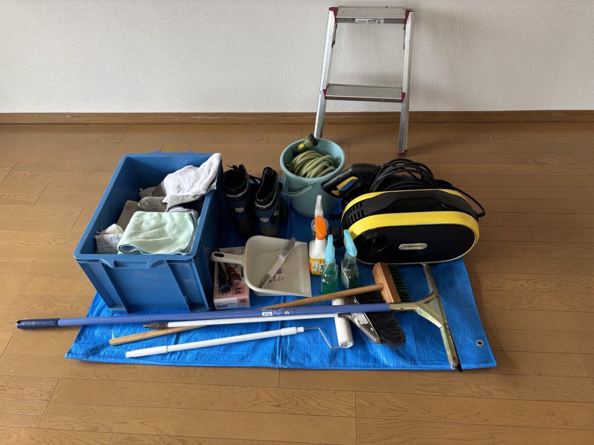 ブルーシートの上に並べた高圧洗浄機やブラシなどハウスクリーニングの道具一式