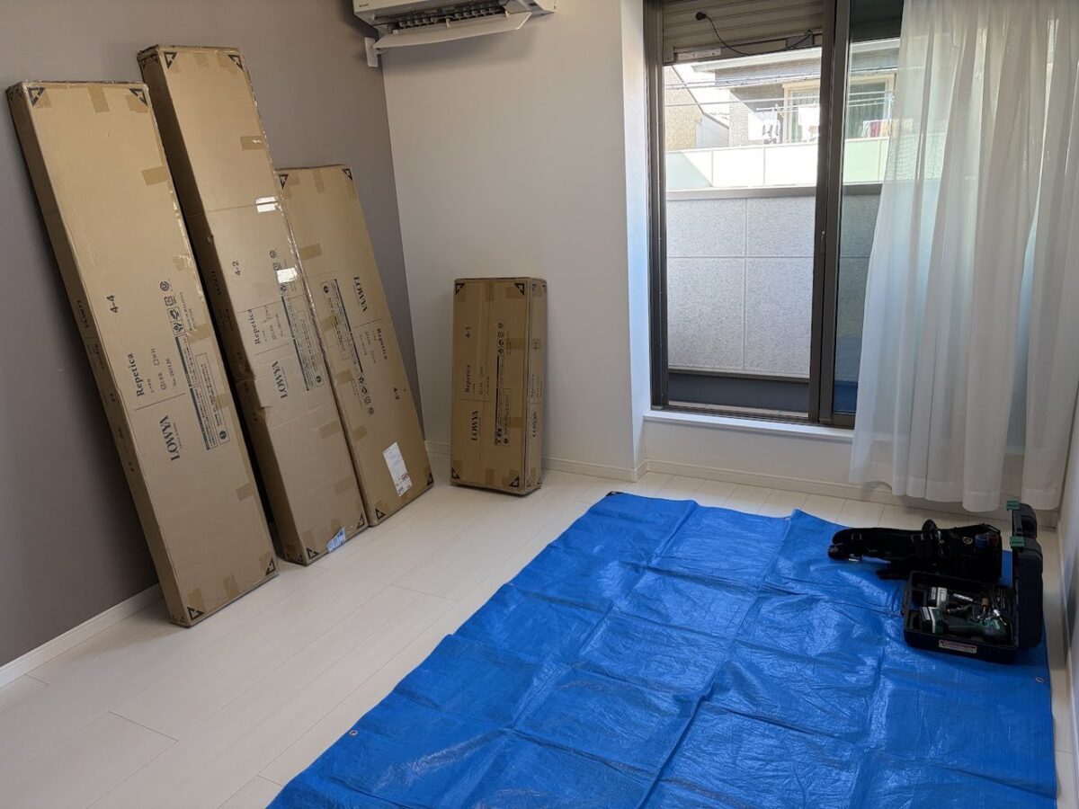 壁際に立てかけた4つのLOWYA家具の梱包と、床に敷いた青い養生シート