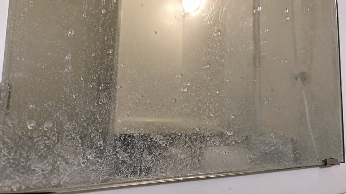 白いウロコ状の水垢と水滴の跡がびっしり付いた浴室の鏡のイメージ